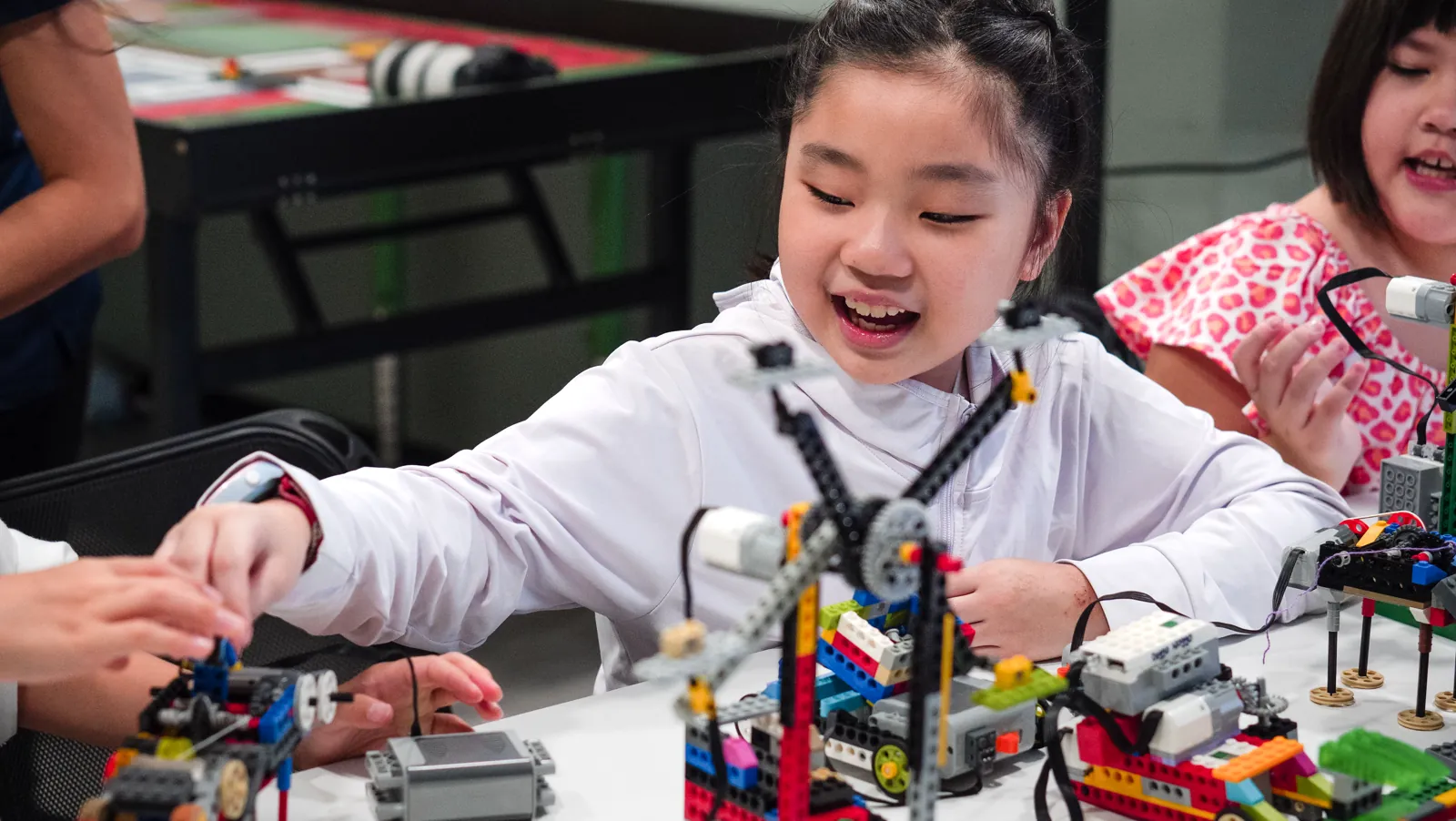 A child smiling with delight as she builds a robotics project alongside other children in a Meta Robotics class